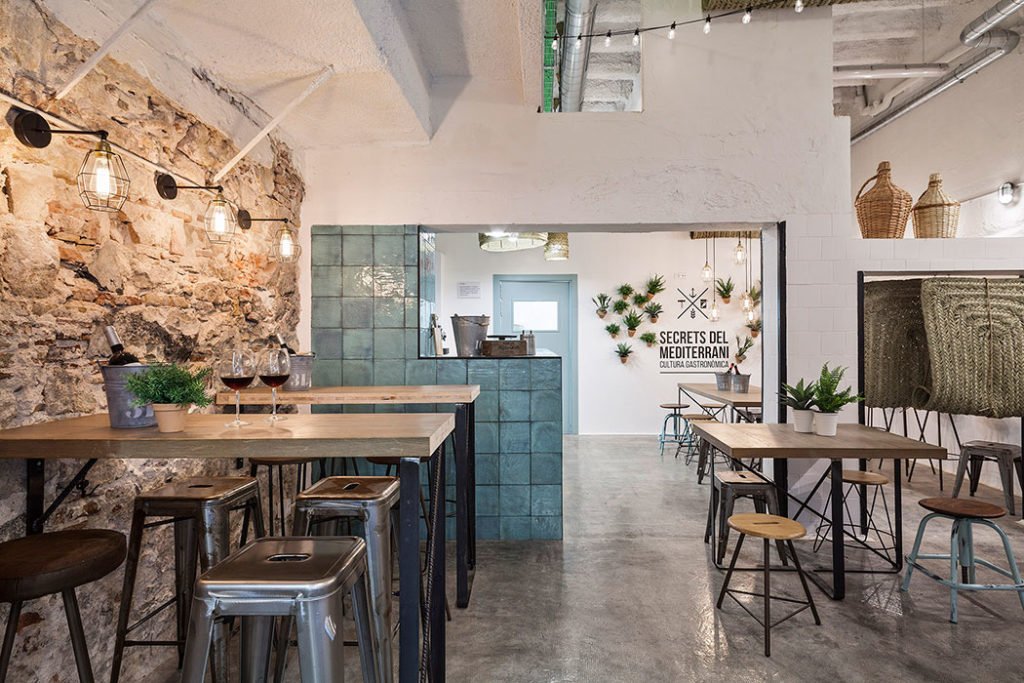 Interior de un local con mesas de madera y paredes de piedra, verticales rectas y luz natural — fotografía de restaurantes Fotointeriores